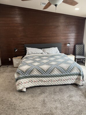 A bedroom with a wooden headboard, a quilted bedspread, a bedside lamp, and a chair. - Blanco House - 3 Bedrooms, 2 Baths, fully furnished house (Liberty Hill)