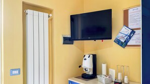 A hotel room with a television, a coffee machine, a bulletin board with information, and a window with curtains. - Camera con Ingresso Indipendente (Agropoli)