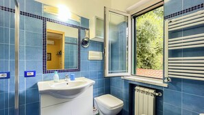 A bathroom with a sink, toilet, bidet, and a window with a view of greenery. - Camera con Ingresso Indipendente (Agropoli)
