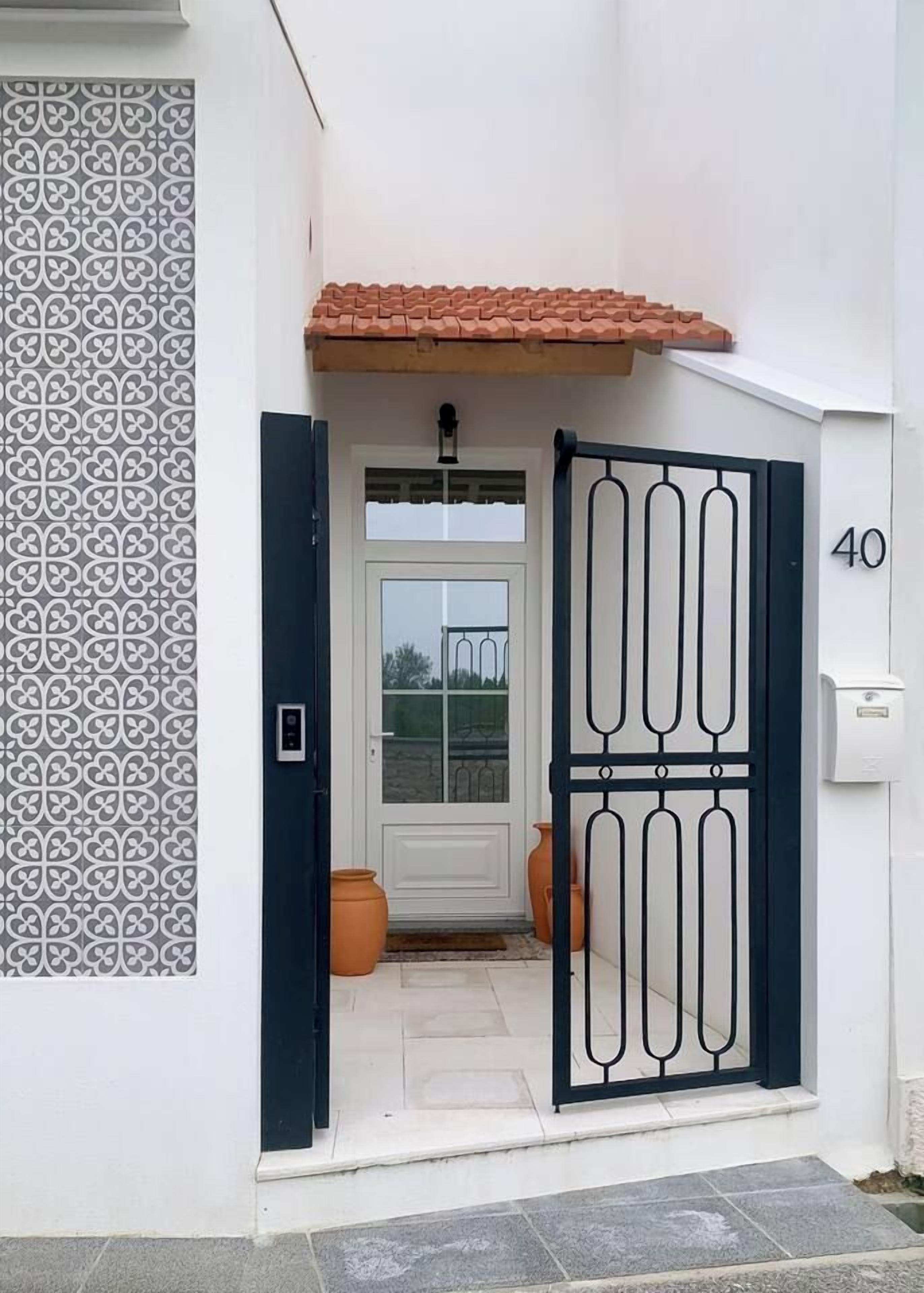 A white building with a patterned wall, a numbered door, and a tiled roof.