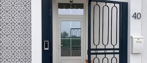 A white building with a patterned wall, a numbered door, and a tiled roof.