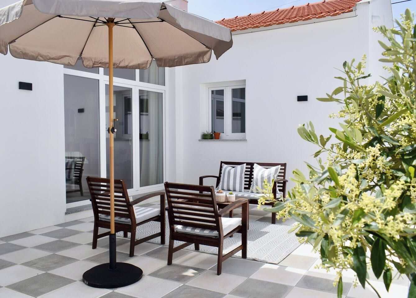 Une terrasse extérieure avec une table et des chaises, un grand parasol et une plante en pot.