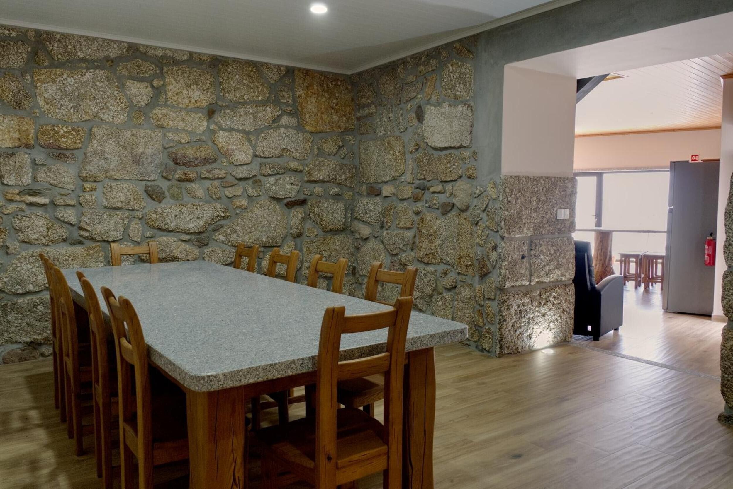 Un espace repas avec un mur en pierre, une table rectangulaire et des chaises en bois.