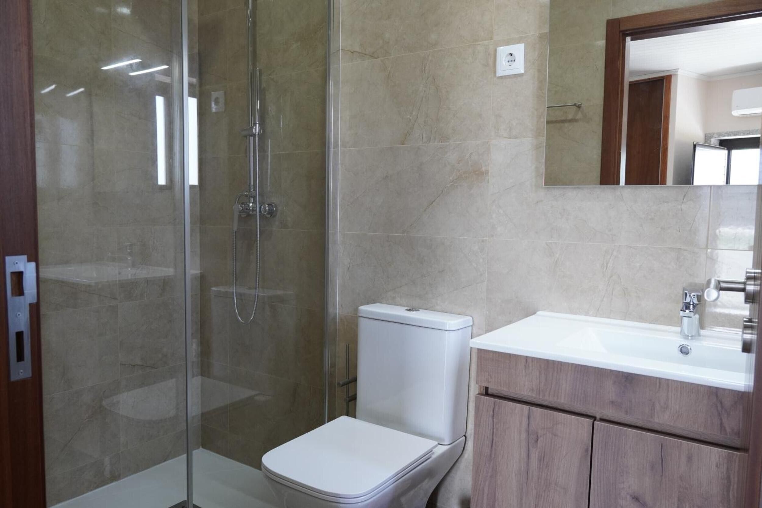 A bathroom with a glass-enclosed shower, a white toilet, and a wooden vanity with a sink.
