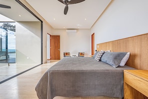 Ein modernes Schlafzimmer mit einem großen Bett, einem Holz-Kopfteil und Blick ins Freie durch eine Glastür.