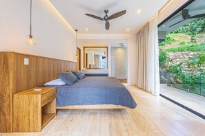 Quarto moderno com cama grande, cabeceira de madeira e vista para um jardim através de uma porta de vidro.