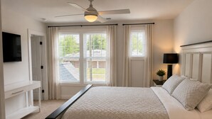 Une chambre à coucher avec un lit, un bureau, un ventilateur de plafond et une fenêtre avec des rideaux.