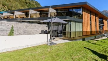 Ein modernes Gebäude mit einer Stein-Fassade, großen Fenstern und einer Holzterrasse mit Sitzgelegenheiten im Freien.