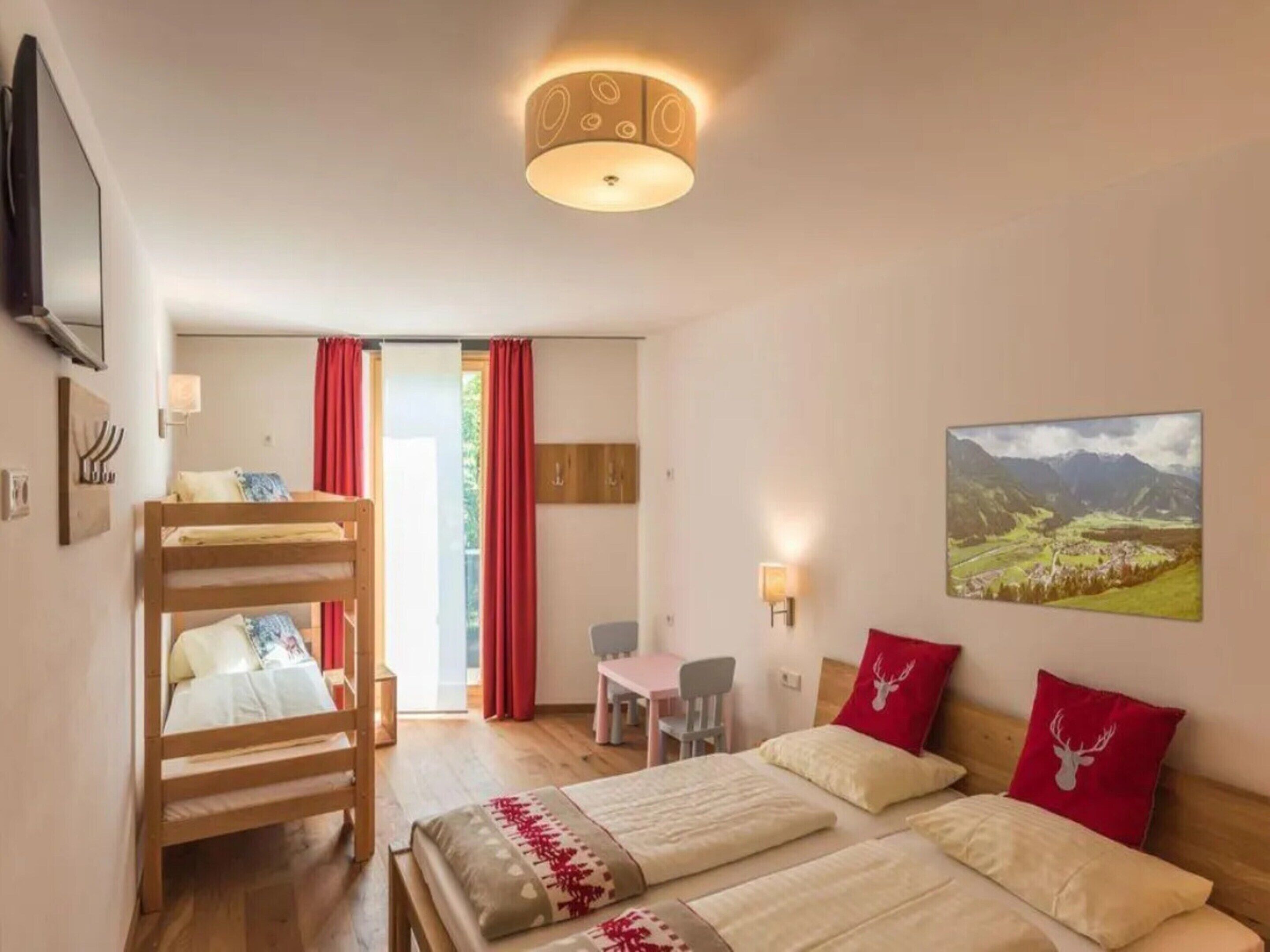A bedroom with a bunk bed, a desk, a chair, a painting, and a ceiling light fixture.