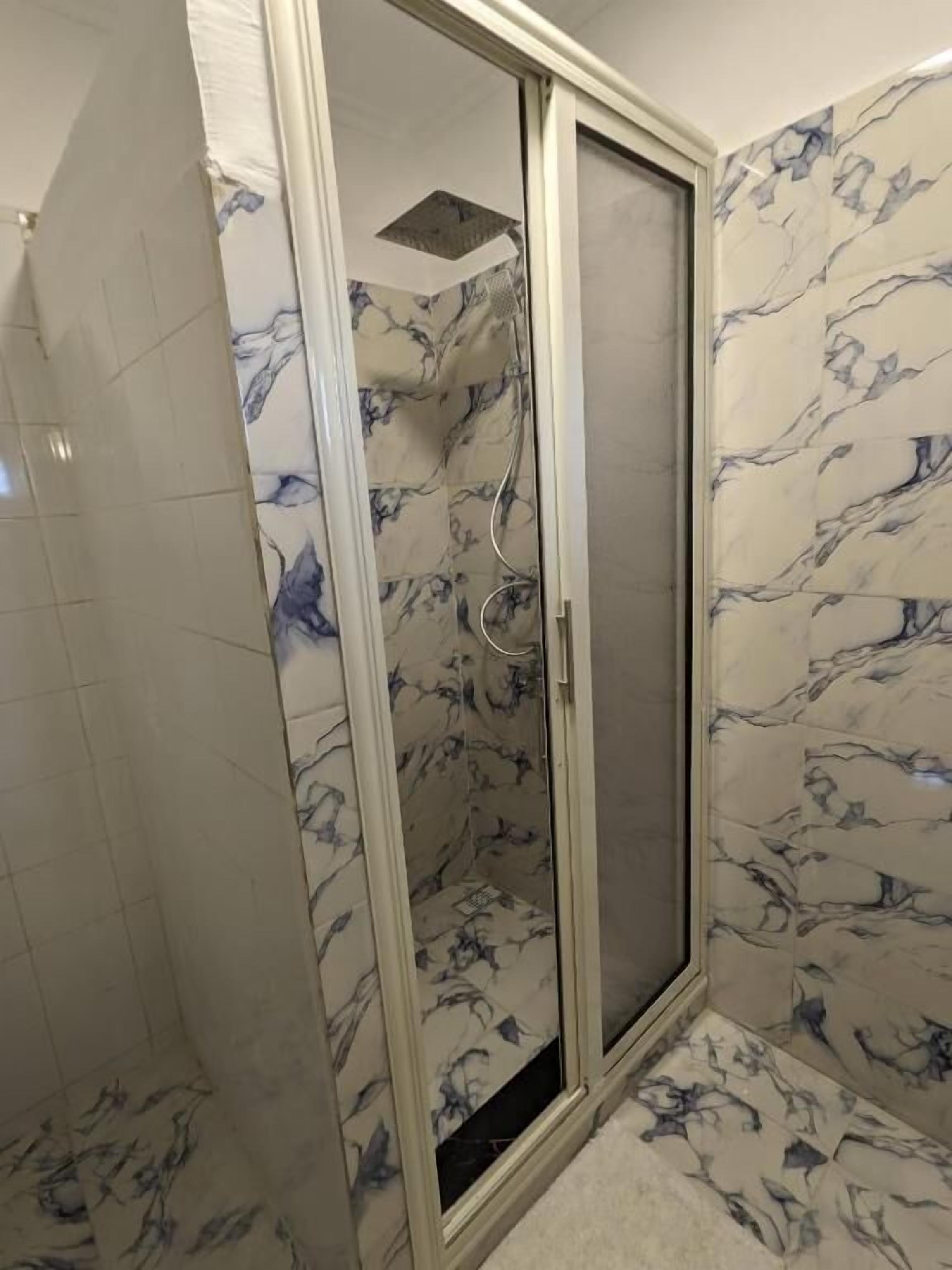 A shower with a glass door, marble wall tiles, and a tiled floor.