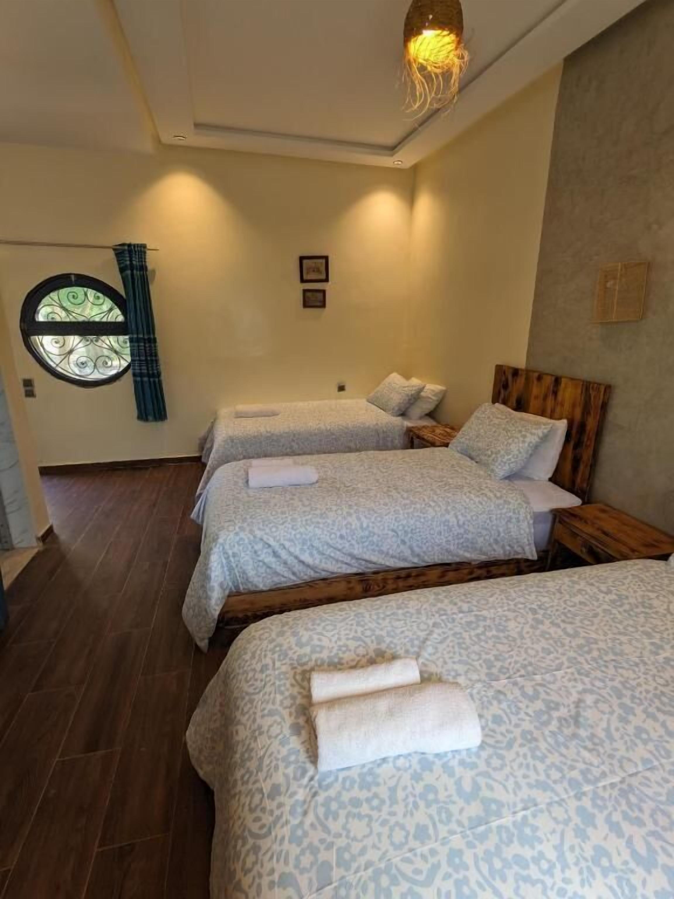 A hotel room with three beds, a circular window, and a wooden headboard.