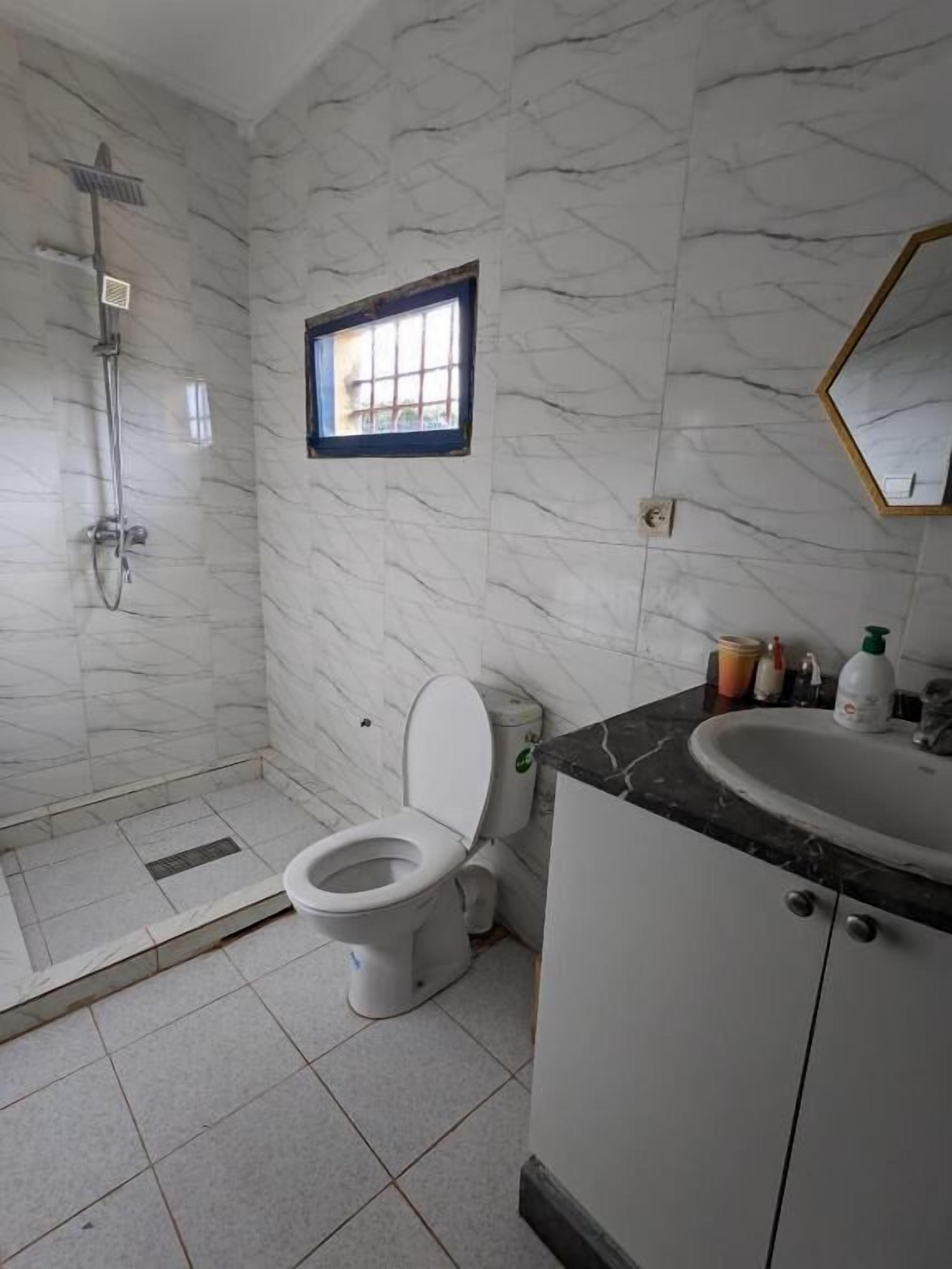 Un baño con ducha, inodoro, lavamanos y ventana.