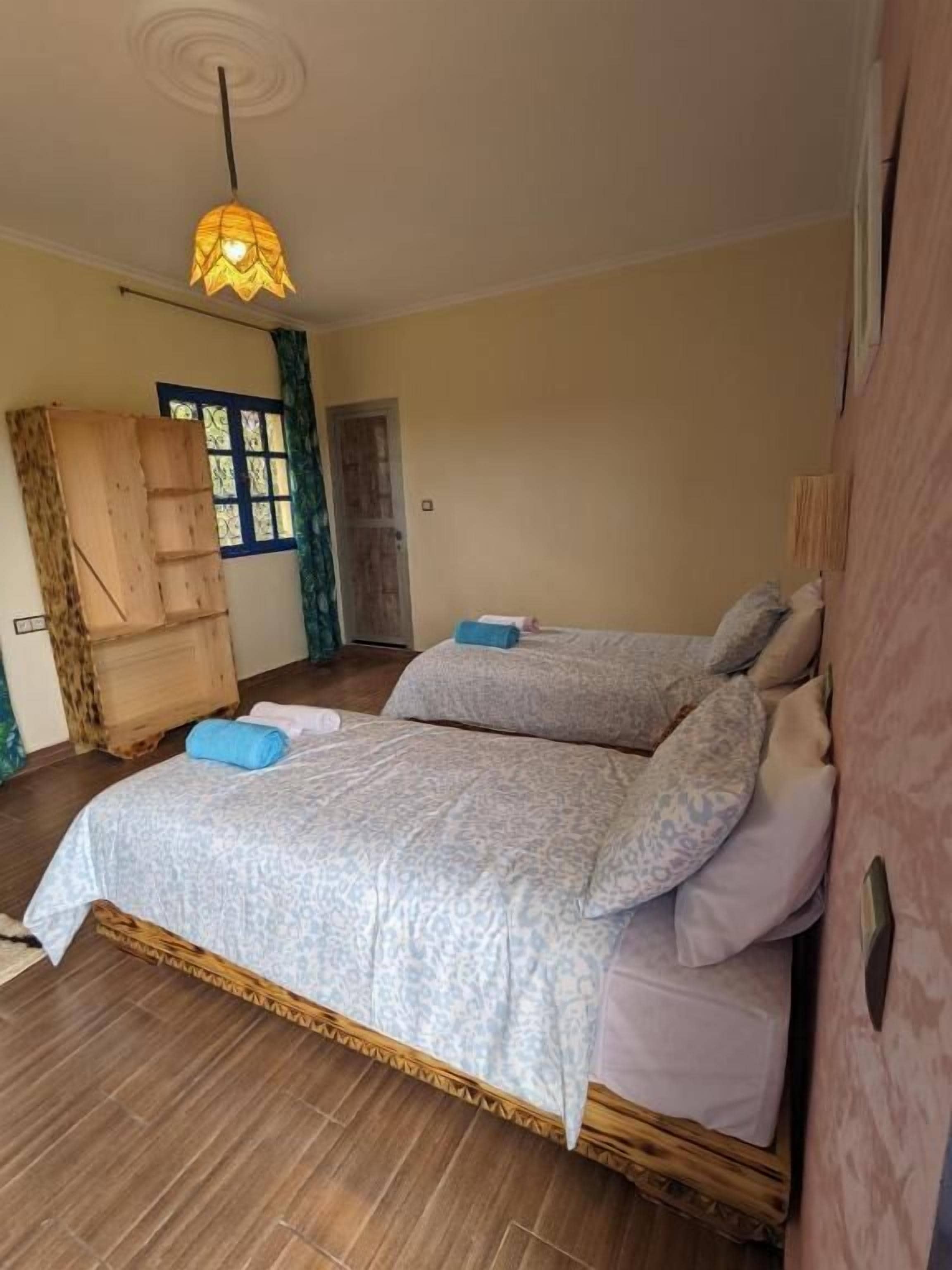 A bedroom with a bed, a wooden wardrobe, and a hanging light fixture.