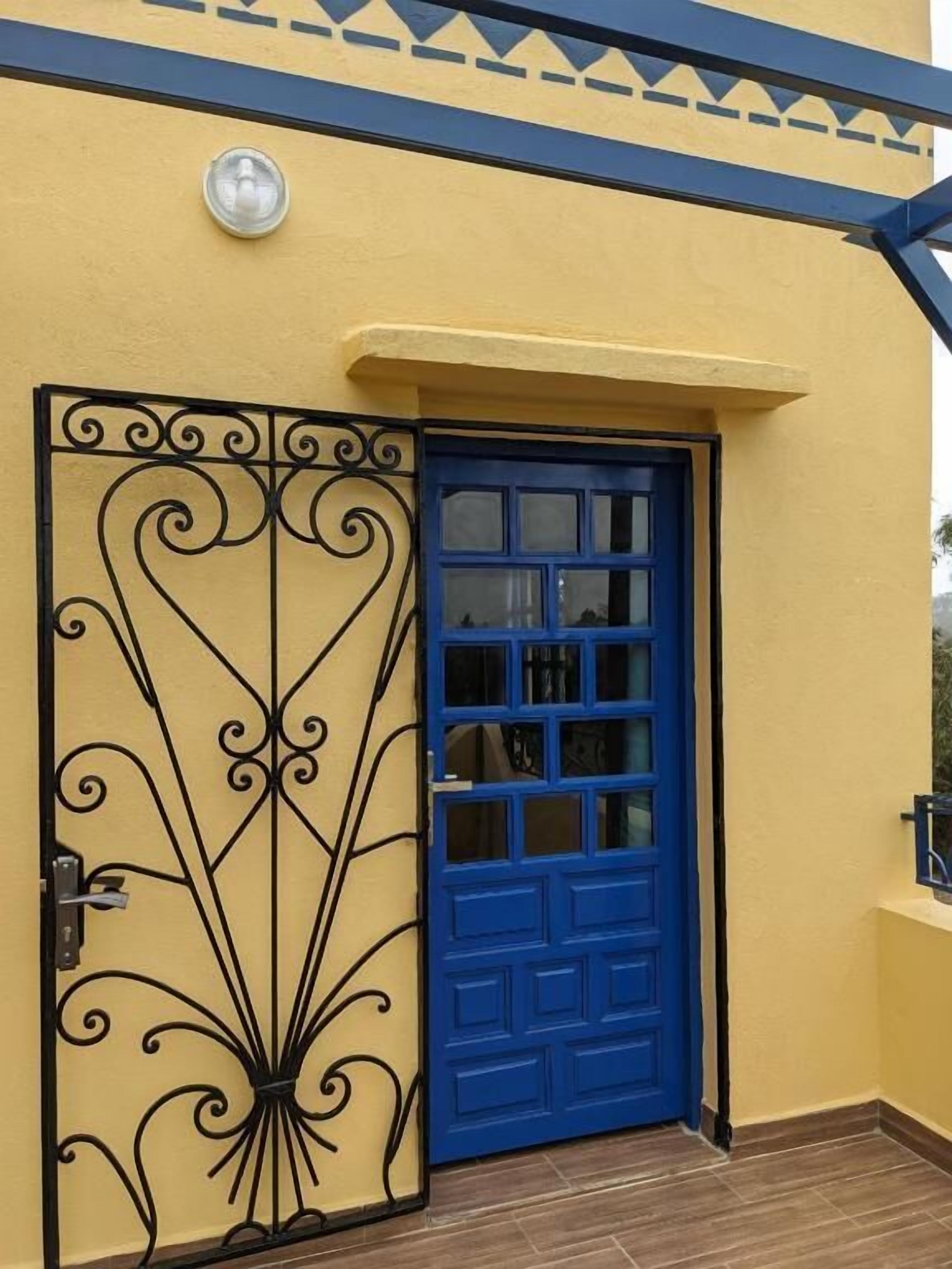 Un bâtiment jaune avec une porte bleue et un portail en métal décoratif.