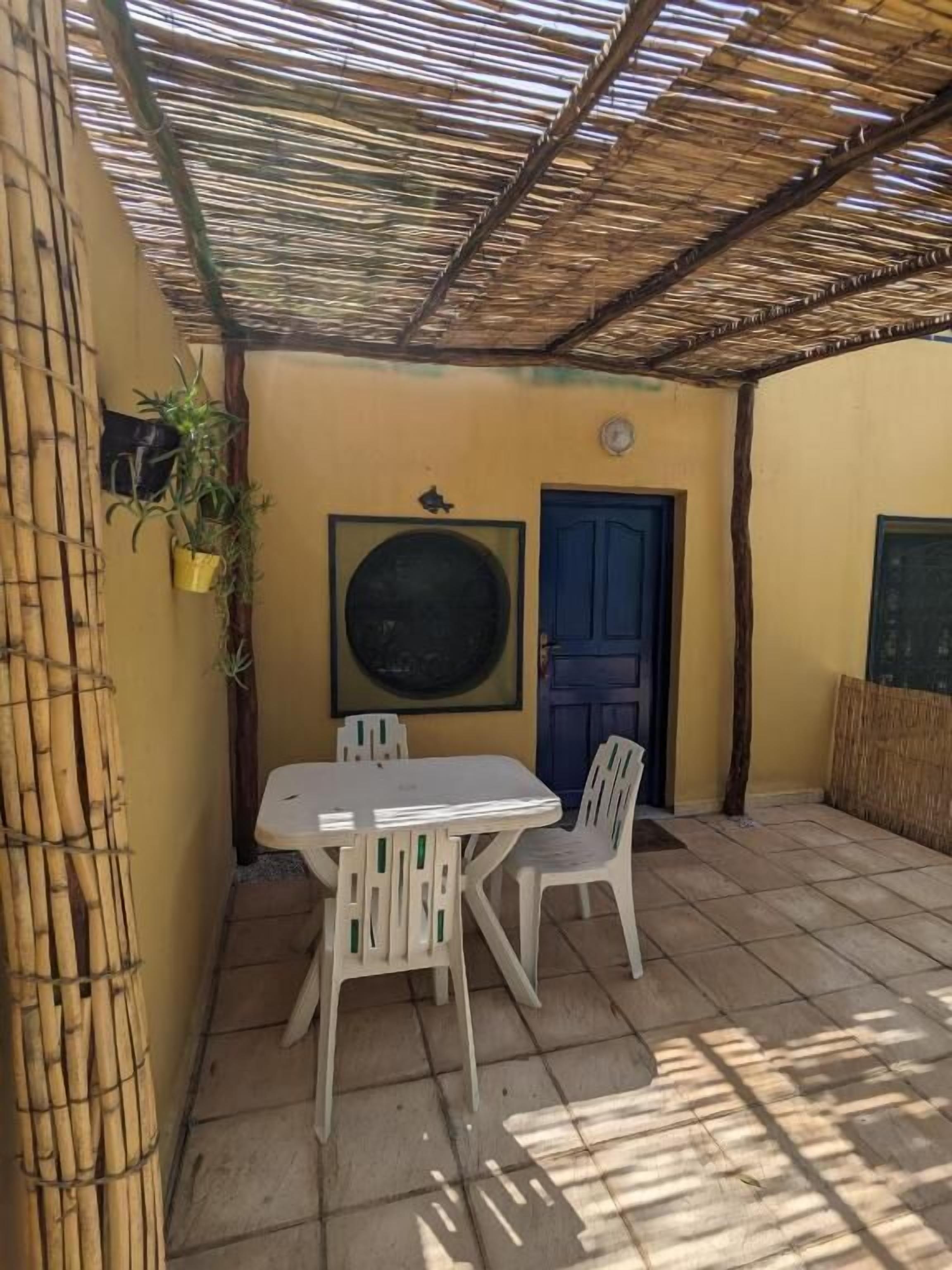 An outdoor patio with a table and chairs, a blue door, and a bamboo structure overhead.