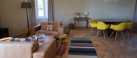 Una sala de estar con un sofá, una mesa de centro, sillas amarillas, una mesa redonda y una alfombra estampada.