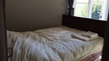 A single bed with a wooden headboard, a window with curtains, and a striped rug on the floor.