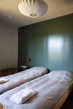 Ein Zimmer mit zwei Betten, einem kleinen Tisch mit Lampe und einer Deckenleuchte.