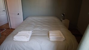A neatly made bed with folded white towels on each side, a bedside table with a lamp, and a door to the left.