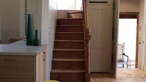 A kitchen with a wooden staircase leading to a door, a dining table with chairs, and a ceiling fan.