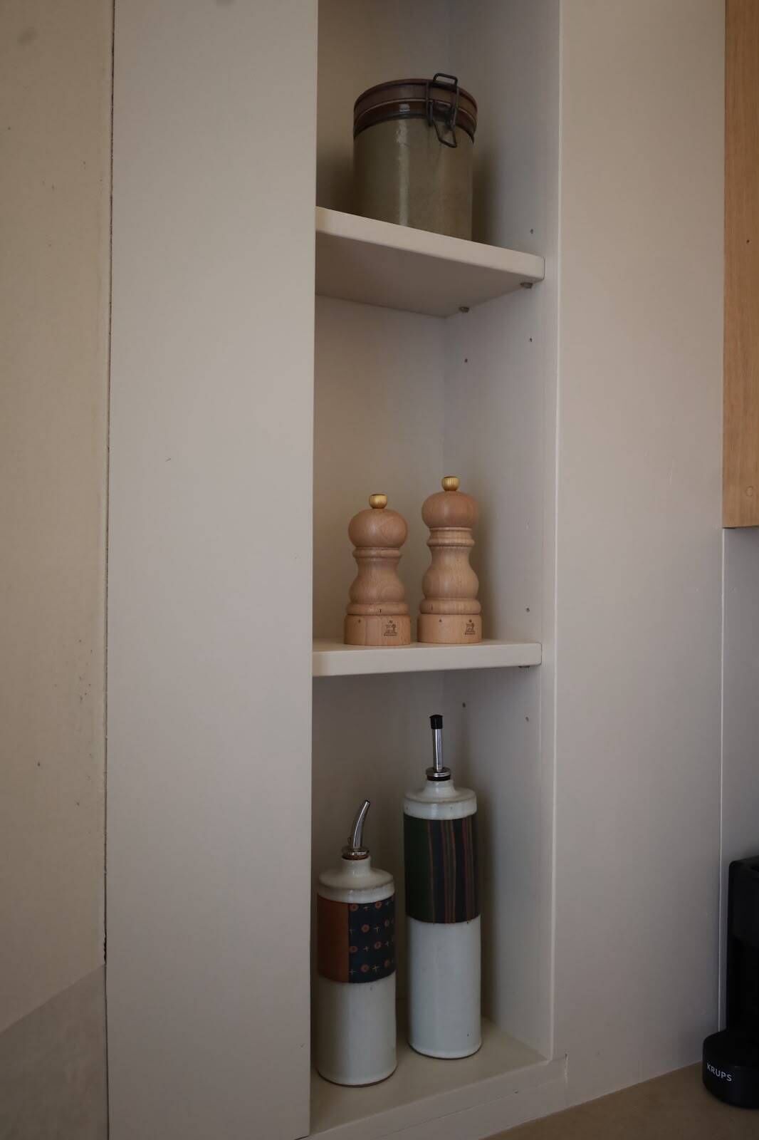 A kitchen shelf with a metal pot, two wooden pepper shakers, and two containers with spouts.