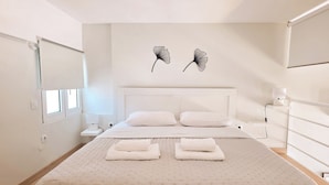 Um quarto com uma cama grande, mesas de cabeceira, um criado-mudo, uma luminária na parede e uma janela.