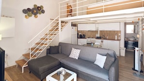 Um apartamento moderno com sofá cinzento, mesa de centro branca, escada de madeira, área de cozinha e ventoinha no teto.