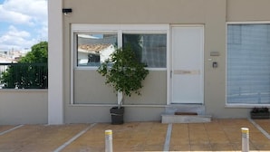 Um edifício com porta branca, janelas grandes e uma pequena árvore em frente.