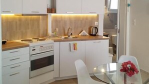 Uma cozinha compacta com armários brancos, uma mesa de jantar de vidro e um sofá em primeiro plano.