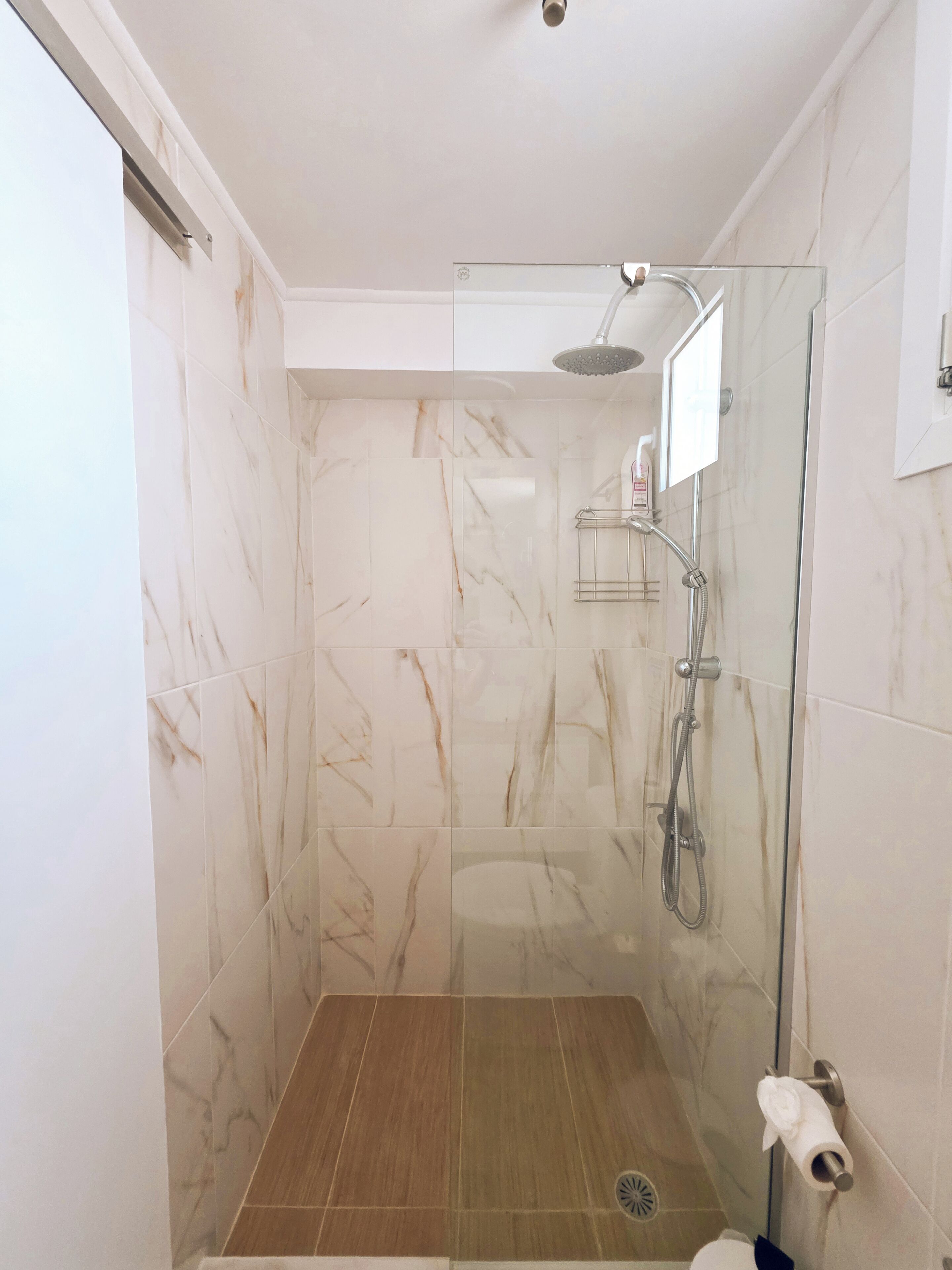A glass-enclosed shower with a handheld showerhead and a wall-mounted faucet.