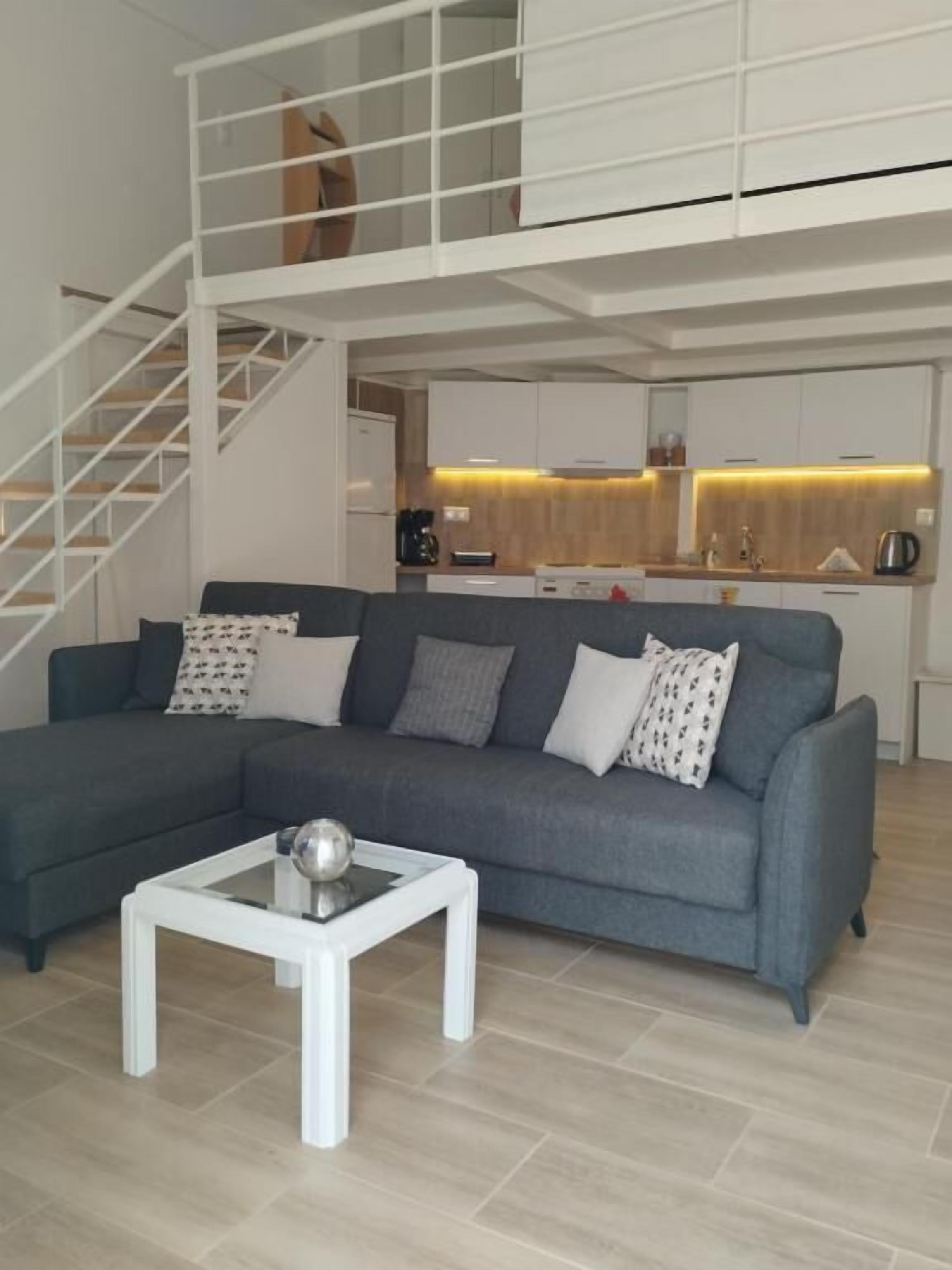 A modern living room with a grey sofa, a white coffee table, and a staircase leading to an upper level.