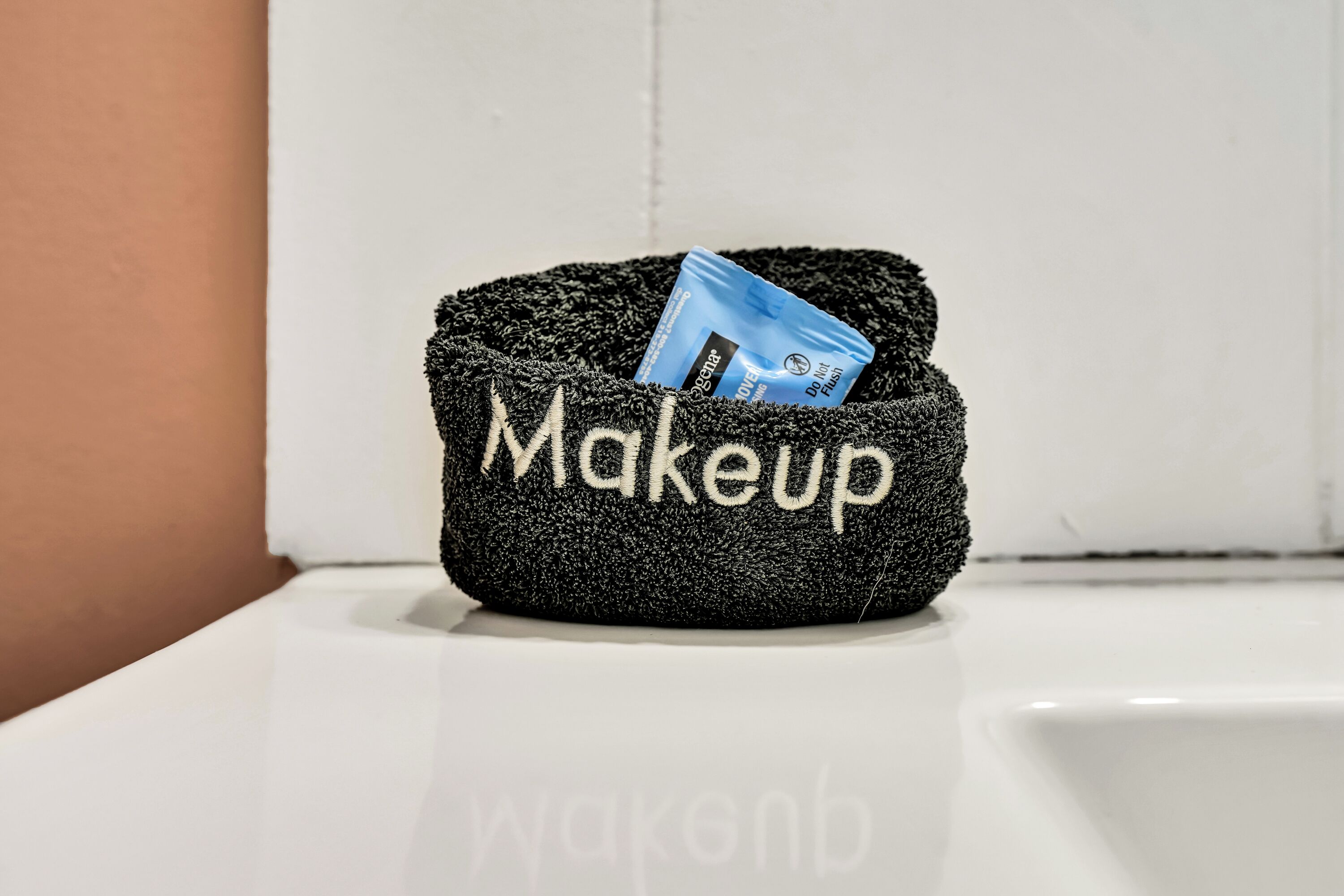 Un sac noir à texture particulière, portant l’inscription « Maquillage », est posé sur une surface blanche.