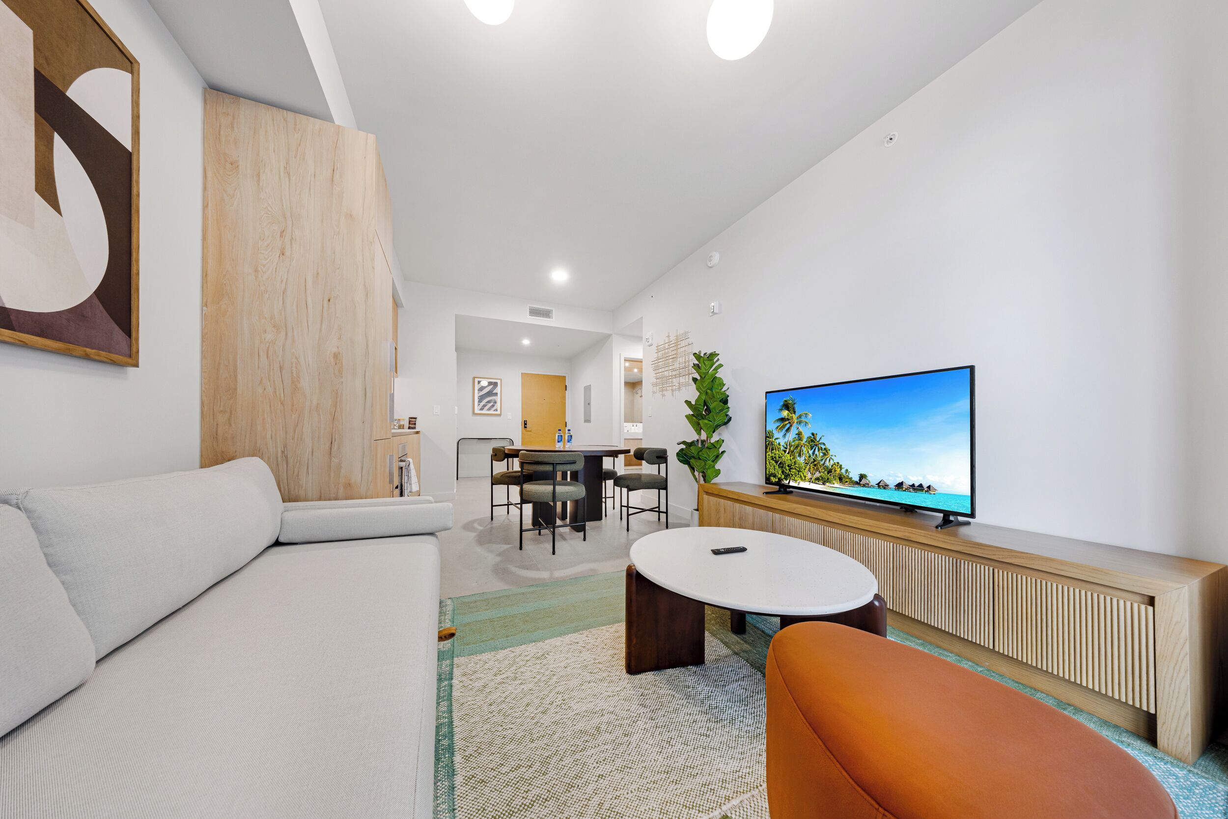 A modern living room with a sofa, a coffee table, a TV, and a dining area with chairs and a table.