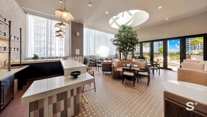 A modern kitchen with a central island, dining area with sofas and tables, and large windows offering views of the city. - 28th-Floor Condo in Miami Worldcenter (Miami)