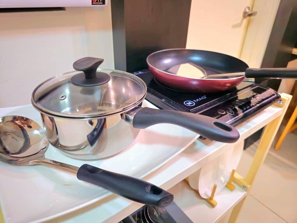 A kitchen with a stove, a frying pan, a pot, and a ladle.