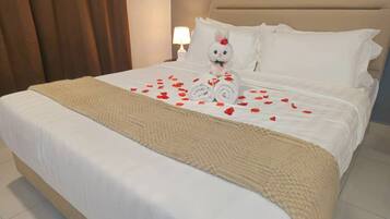 A neatly made bed with a rolled towel, a plush toy, and rose petals on the bed.
