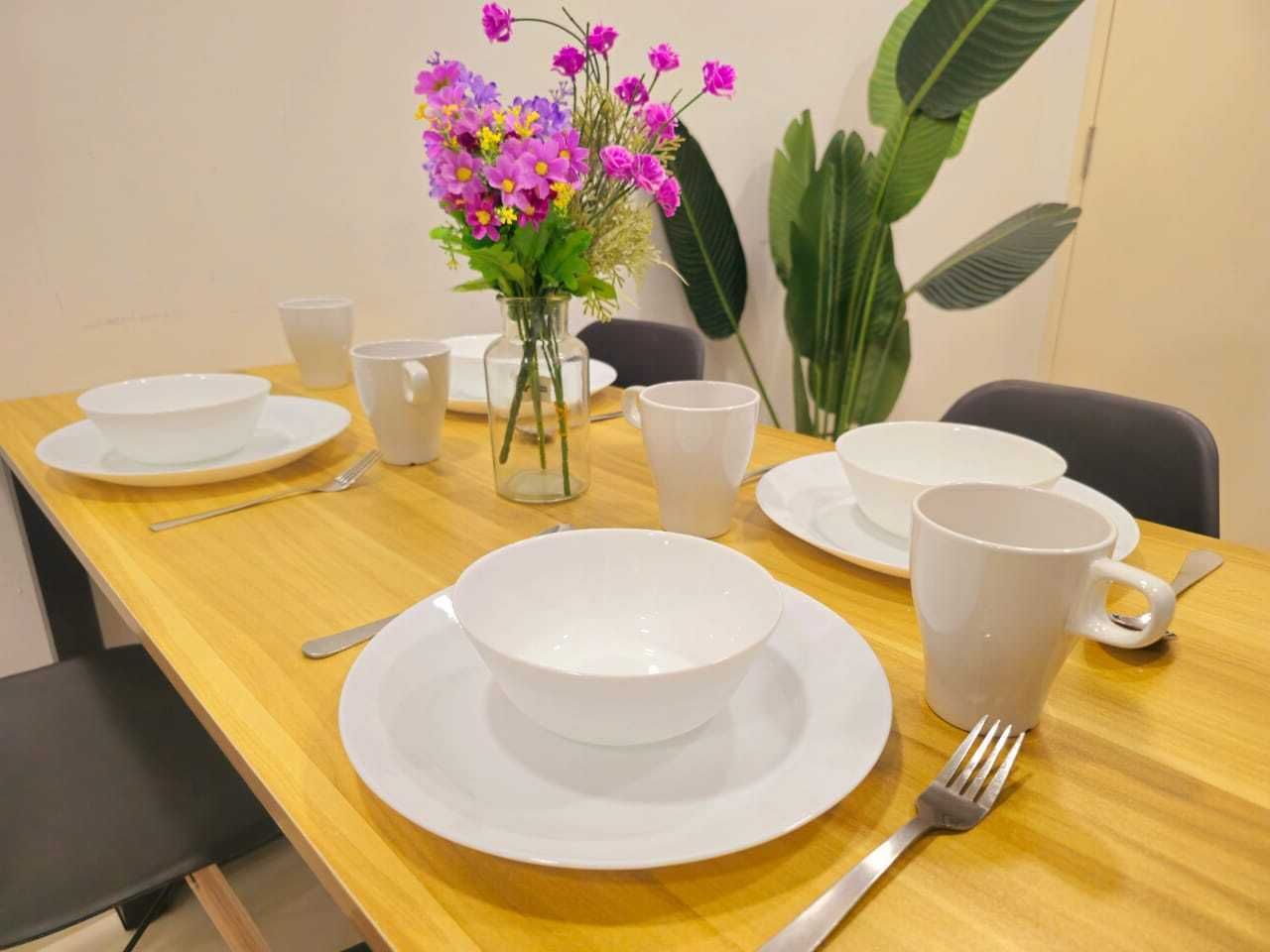 A dining table set with white plates, bowls, and cups, accompanied by a vase of flowers.