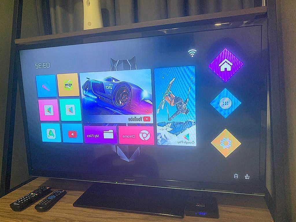 A flat-screen TV with a digital interface, remote controls, and a wooden frame.