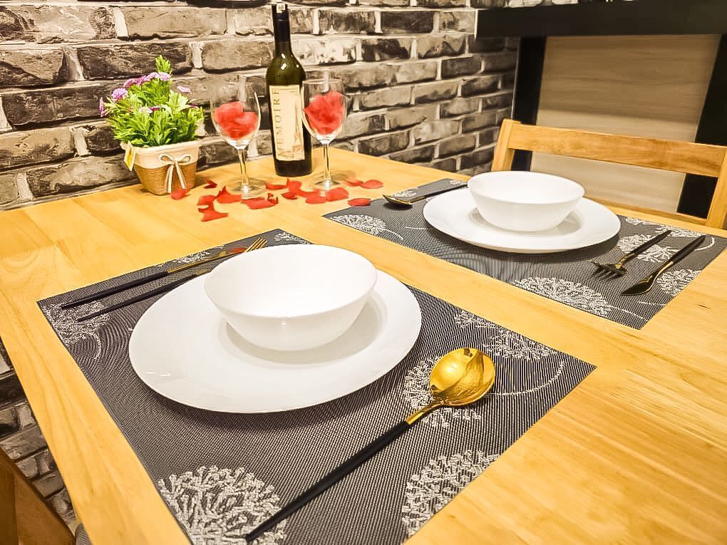 Une table de salle à manger en bois, avec deux assiettes blanches, une bouteille de vin et un verre de vin rouge.