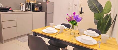 A dining area with a wooden table set for four, white plates, cups, and a vase with purple flowers.