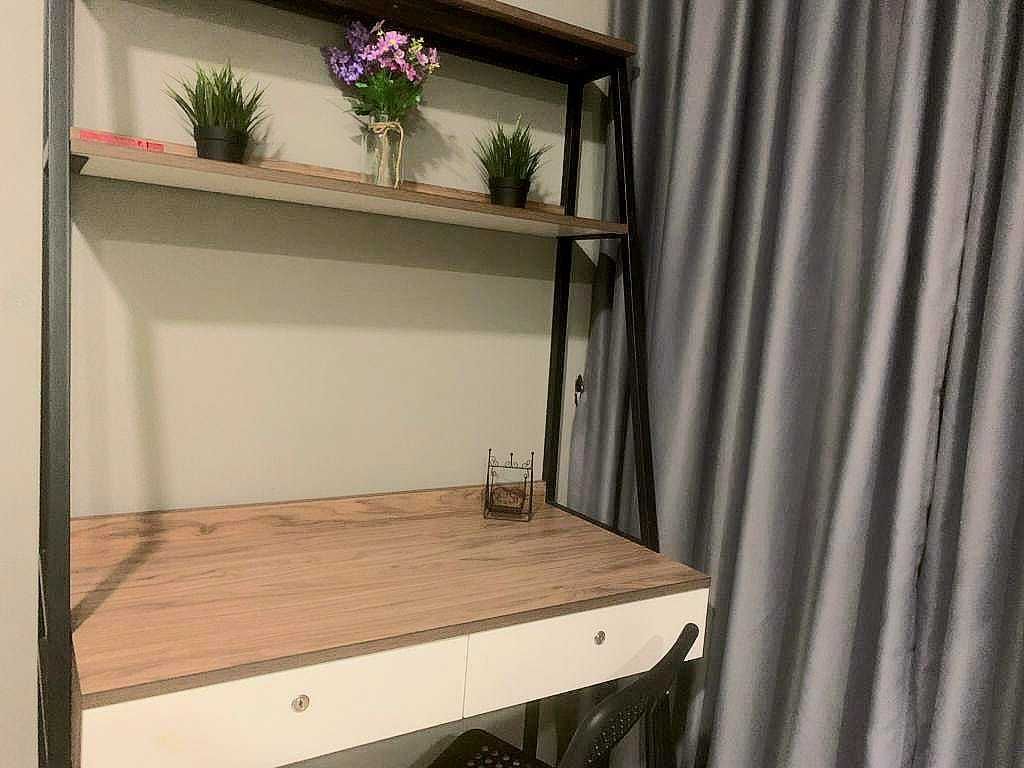 A desk with a wooden top, a white drawer, and two shelves with plants.