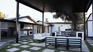 Un patio trasero techado con una parrilla, asientos y vistas al jardín.