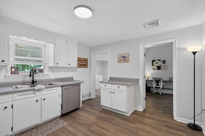 A kitchen with white cabinets, a dishwasher, and a window with blinds.