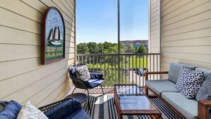 Ein überdachter Balkon mit Blick auf eine grüne Landschaft, ein Korbsessel, eine Couch und ein Schild mit der Aufschrift 'Coldest Drinks On the Islands'.