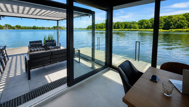 Ein modernes Zimmer mit großem Fenster mit Seeblick, einem Holztisch und einer Couch.