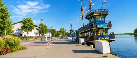 A waterfront promenade with a row of traditional boats docked, a clear sky, and a calm river.