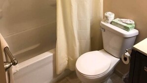 Une salle de bain avec un rideau de douche, des toilettes et une étagère où sont pliées des serviettes.