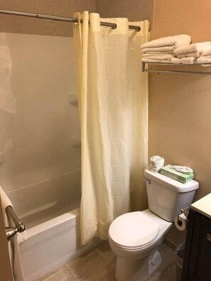 Un baño con cortina de ducha, inodoro y repisa con toallas dobladas.