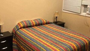 Une chambre à coucher avec un lit, une table de chevet, une lampe et une fenêtre avec des stores.