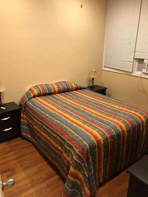 Un dormitorio con cama, mesita de noche, lámpara y ventana con persianas.